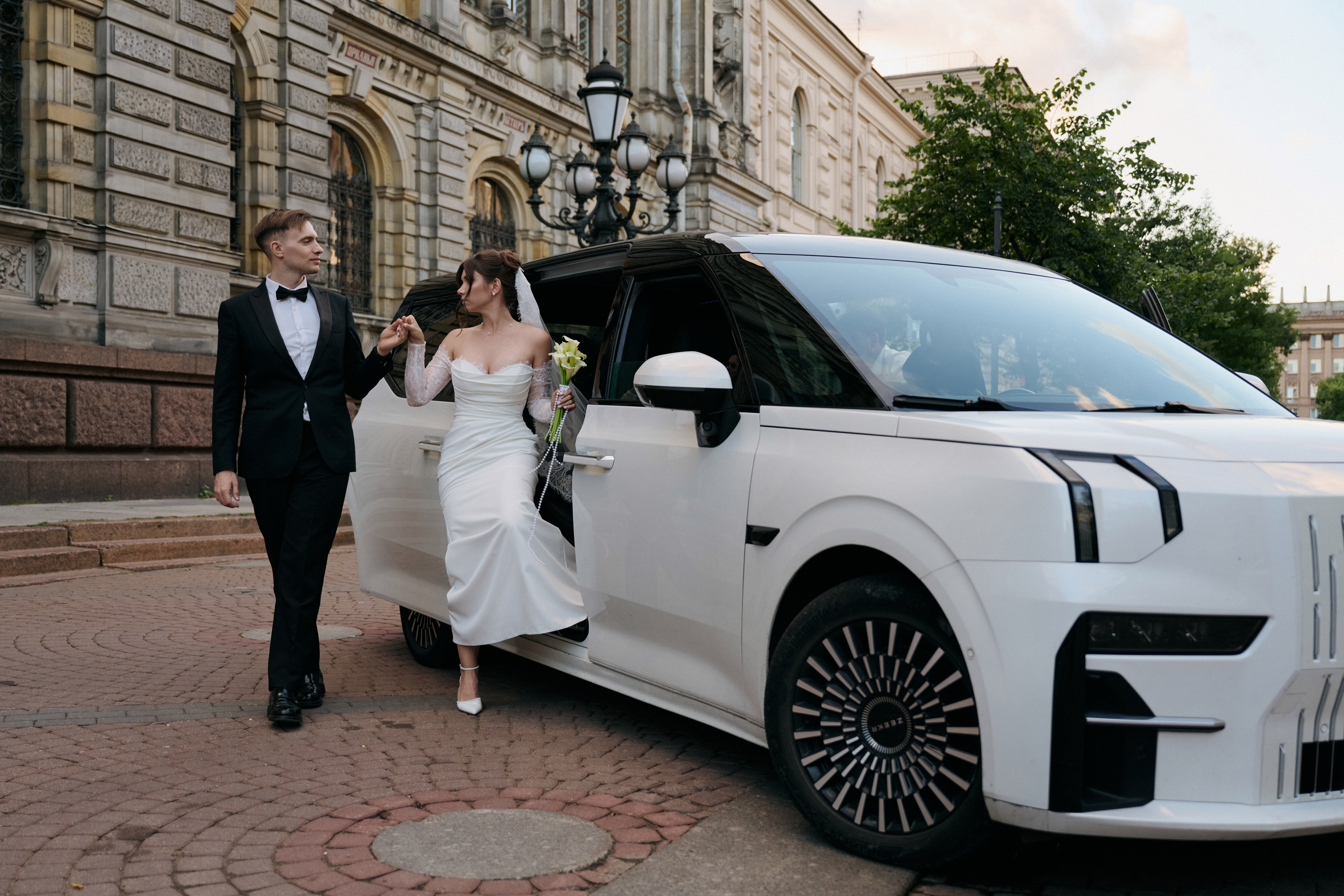 Жених помогает невесте выйти из белого автомобиля