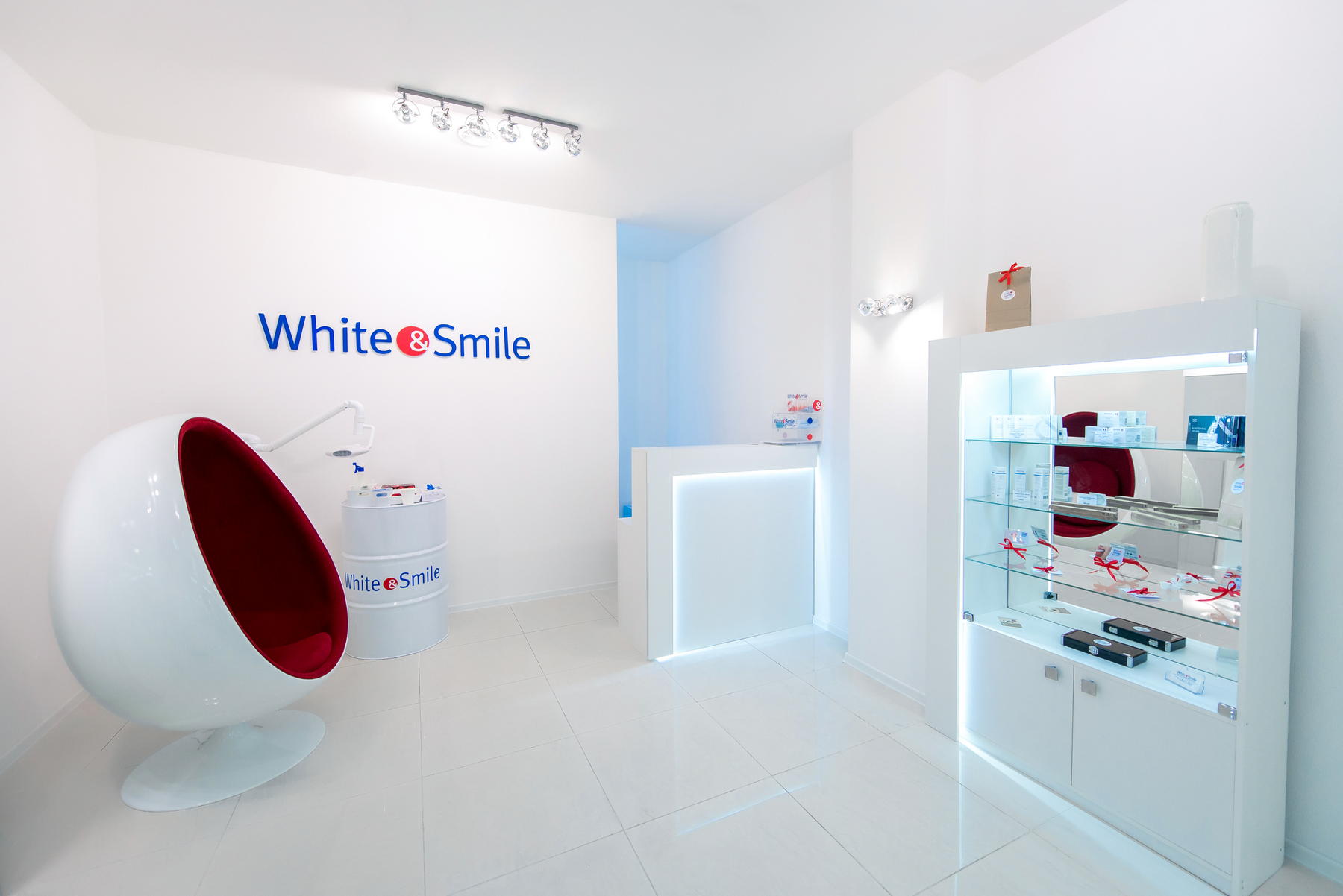 Светлый интерьер White&Smile с красным креслом, подсвеченной стойкой и витриной.