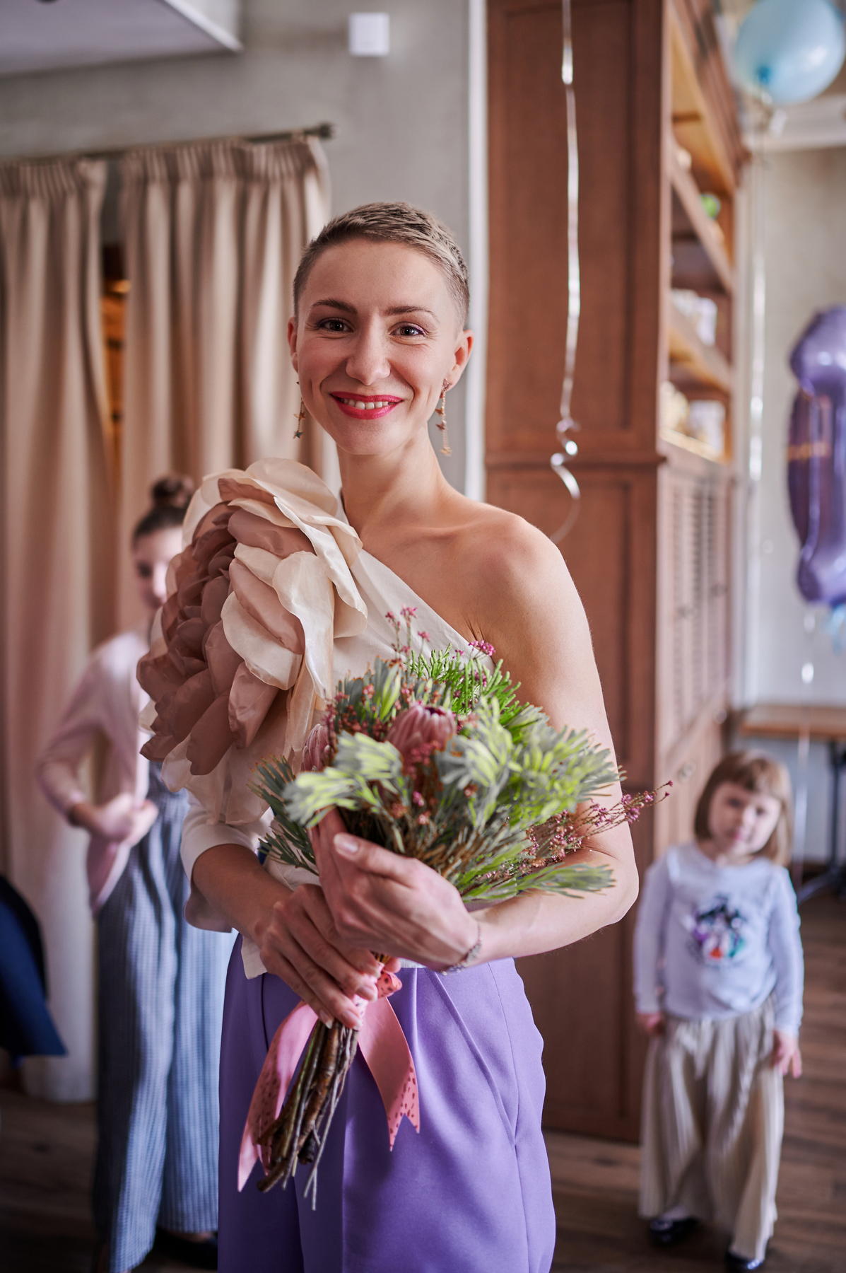 Улыбающаяся женщина держит букет возле входа