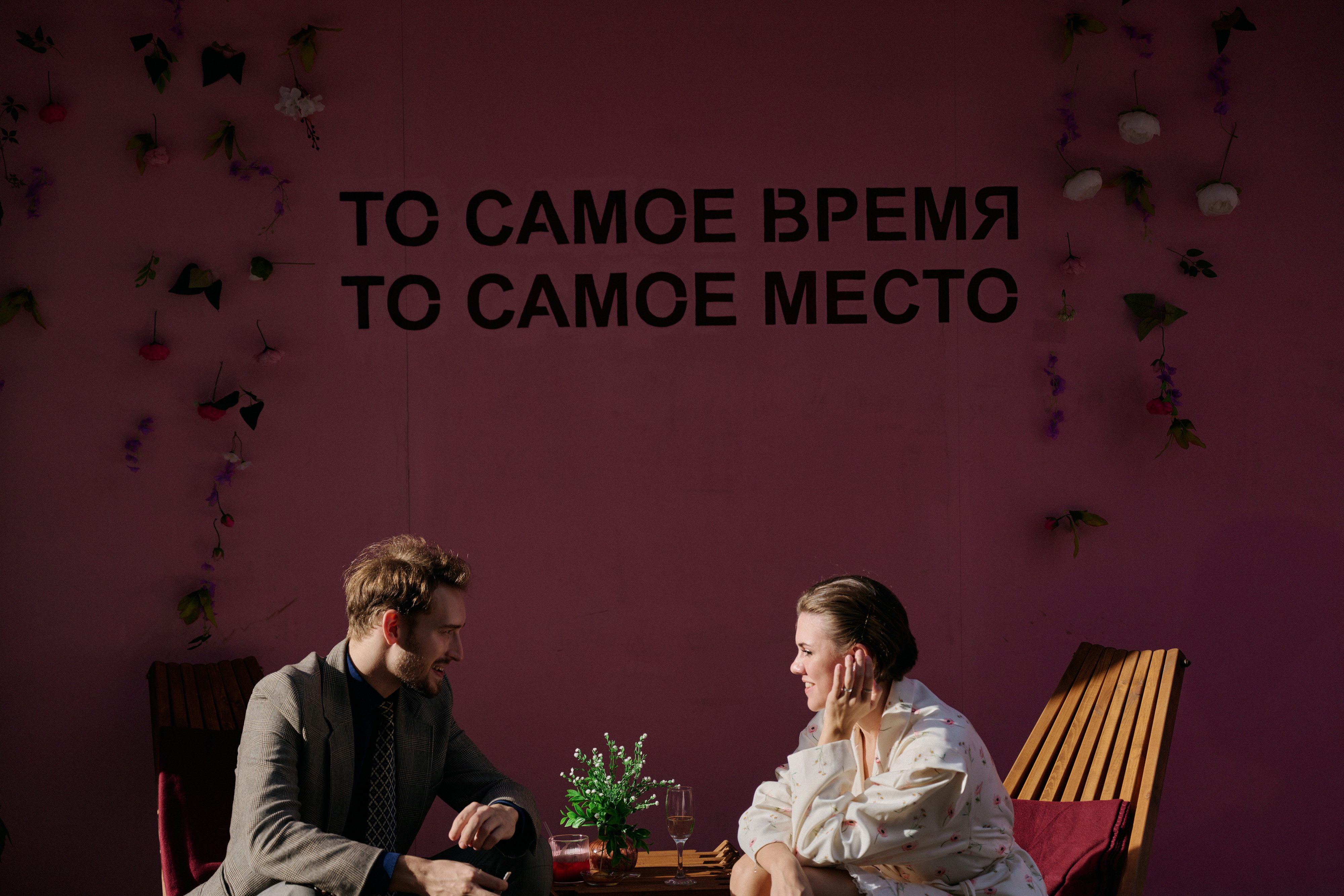 Невеста и жених разговаривают за столиком у розовой стены
